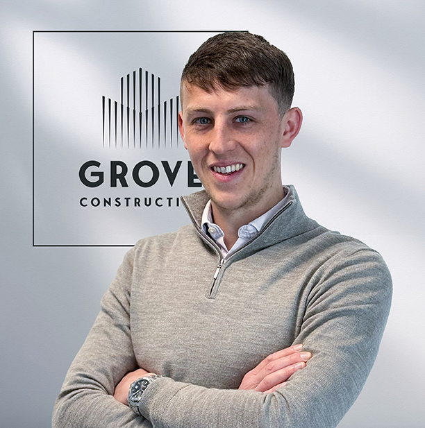 Portrait of a smiling man with arms crossed, standing in front of a Grove Construction sign.